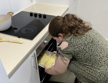 Cook top and oven with woman bending down to putt food tray in to the oven